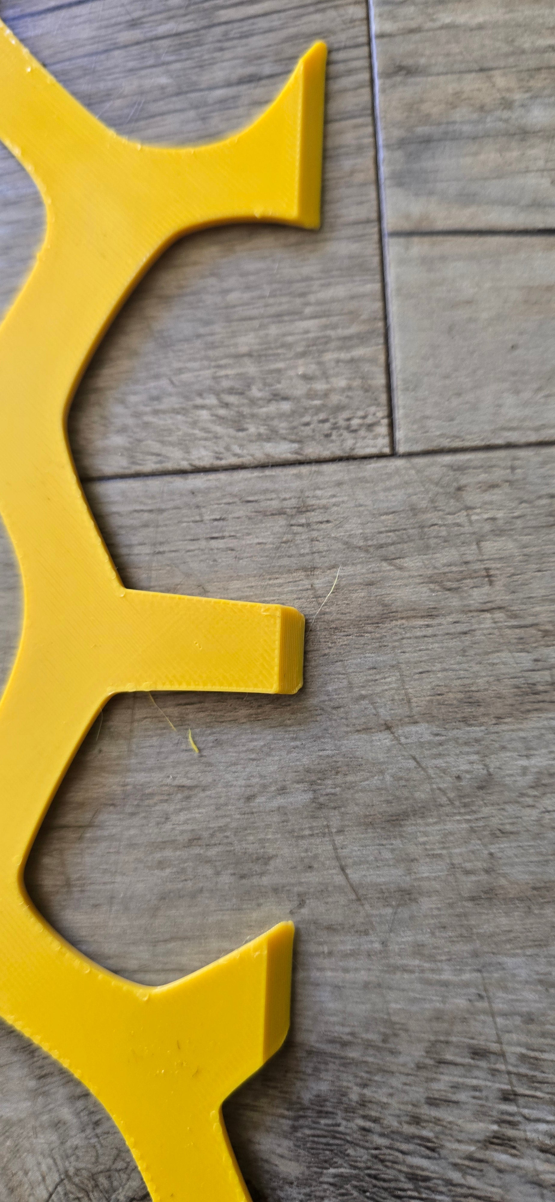 Close up of a 3D printed geometric wall panel in vibrant yellow showing crisp edge details on a wooden background