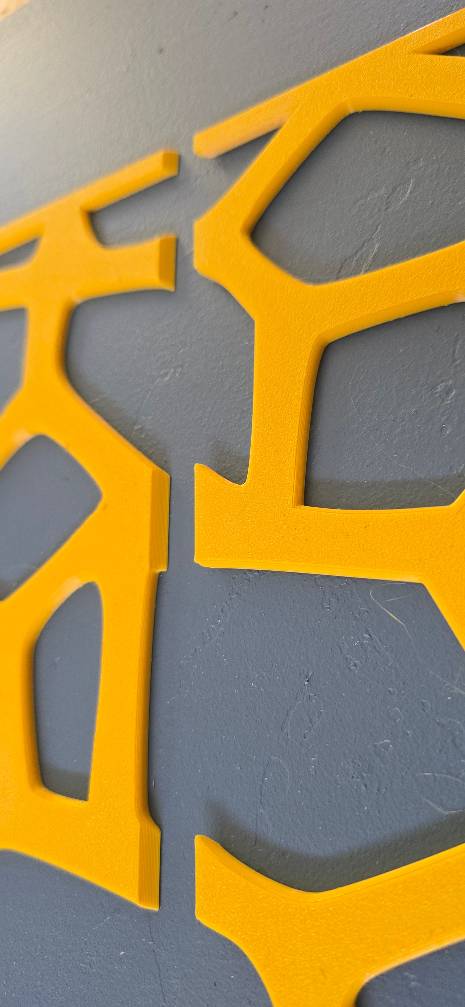 Two yellow 3D printed fretwork furniture panels side by side showing the textured surface finish against a dark blue wall