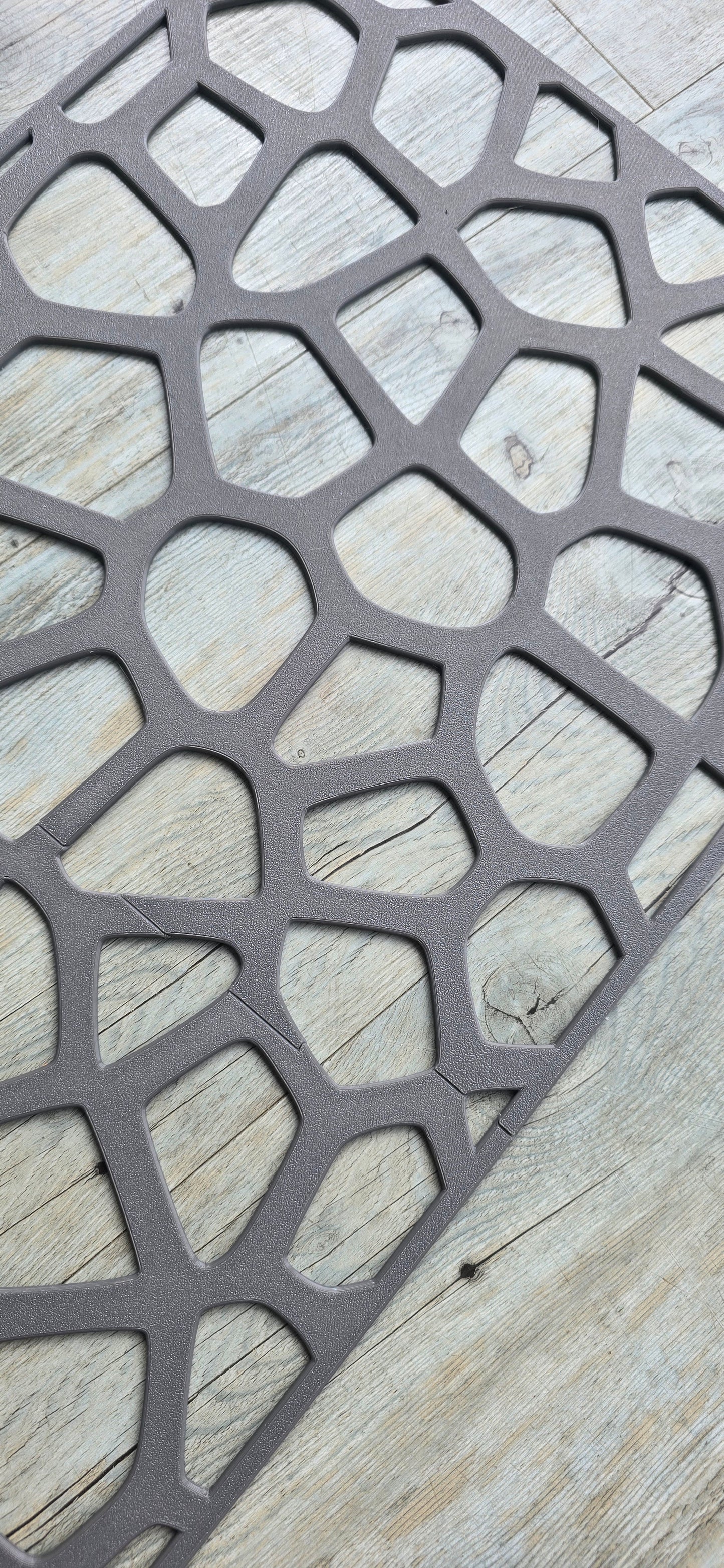 A grey textured geometric voronoi pattern wall panel resting flat on a light wood grain floor surface