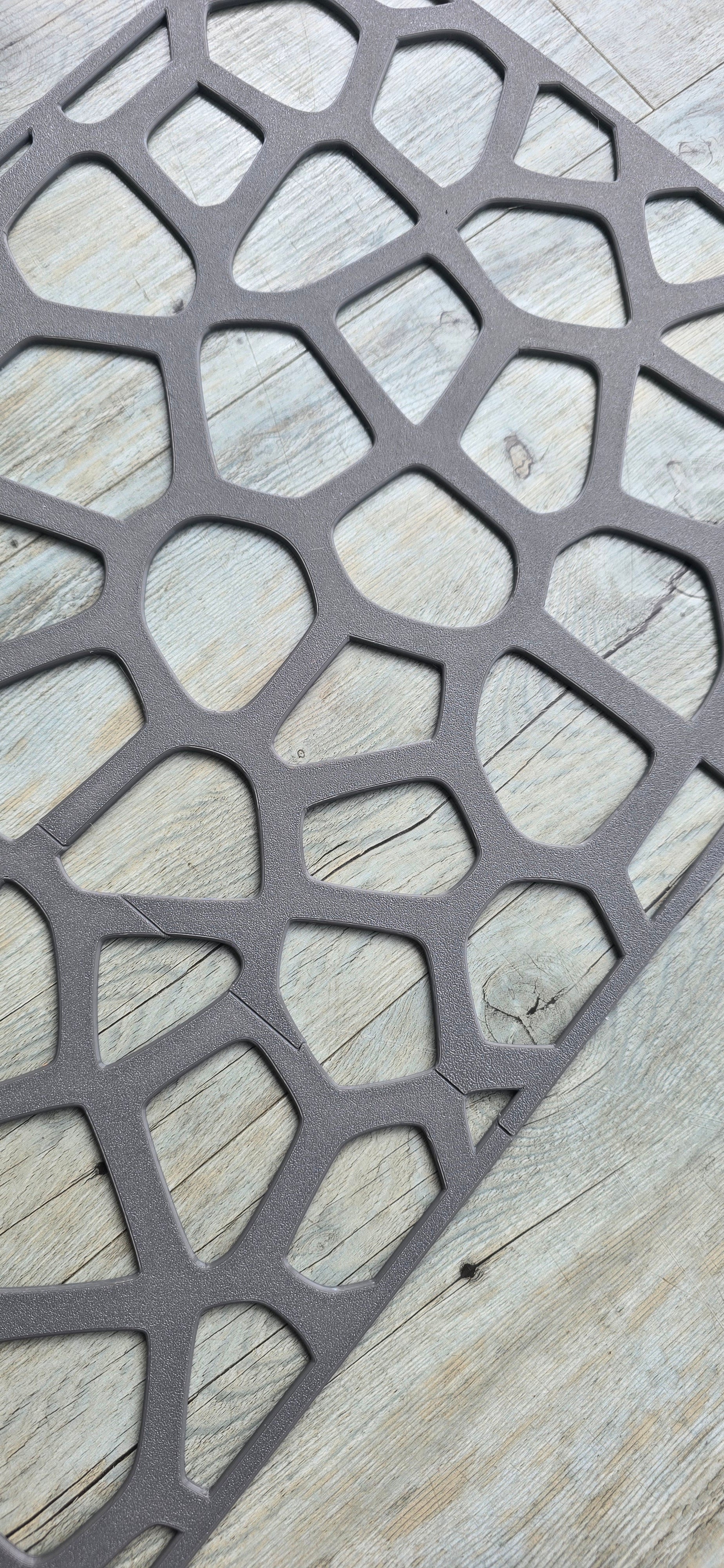 A grey textured geometric voronoi pattern wall panel resting flat on a light wood grain floor surface